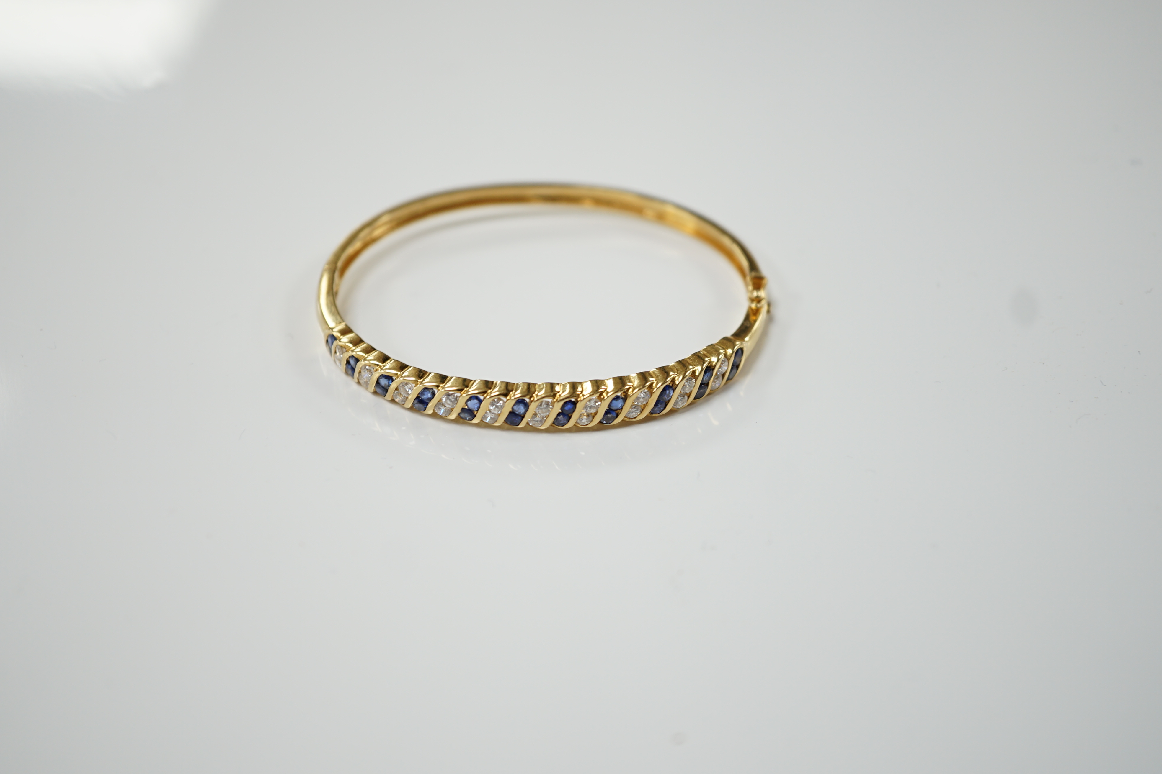 A 750 yellow metal, sapphire and diamond cluster set hinged bangle, interior diameter 56mm